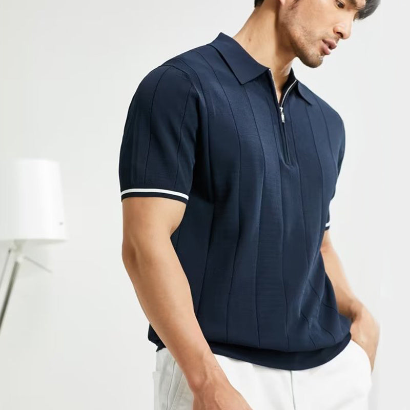 Man wearing a navy blue polo shirt with white pants on a light gray background
